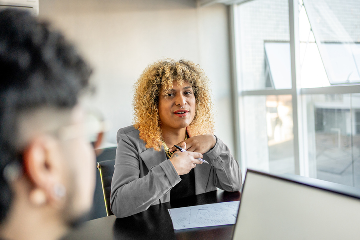 Image of a trans woman with curly hair sitting in a business meeting