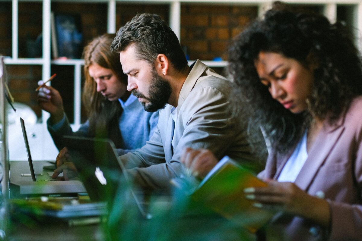 Three people sitting at at a desk reading their computers 